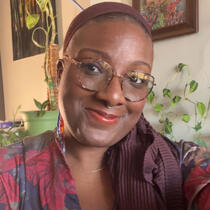 this a photo of Bre. The background is of a lake. Bre is wearing a white shirt and has locs in her hair.